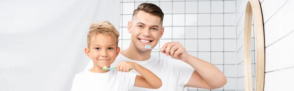 Fils et père souriants tenant des brosses à dents et regardant la caméra, bannière — Photo de stock