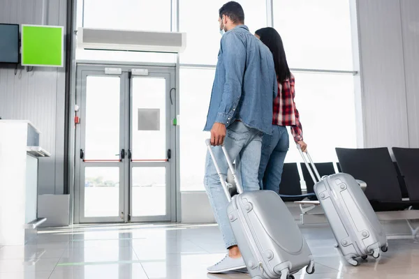 Pareja interracial caminando con el equipaje en la sala de salida - foto de stock