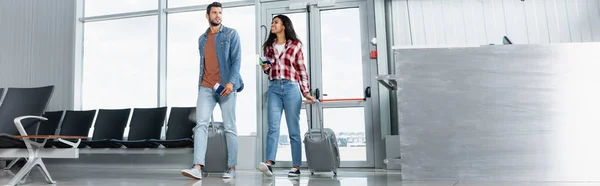 Happy multicultural couple walking with luggage and passports in airport, banner — Stock Photo