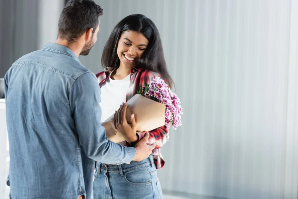 Man holding wrapped flowers near african american girlfriend in airport — Stock Photo
