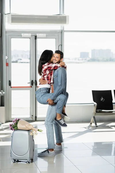 Щасливий чоловік тримає в руках афроамериканку під час зустрічі в аеропорту — стокове фото