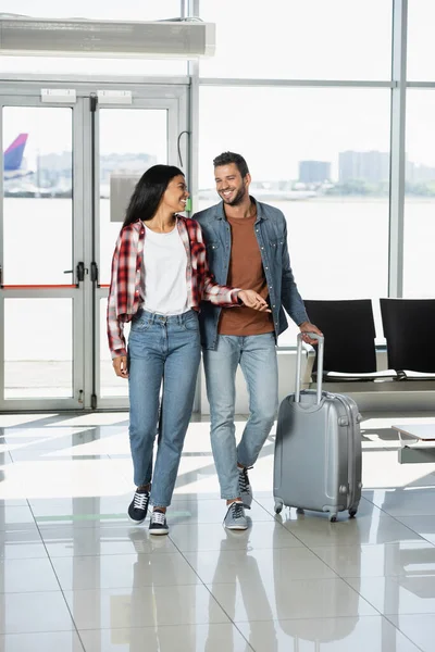 Happy multicultural couple with luggage walking in airport — Stock Photo