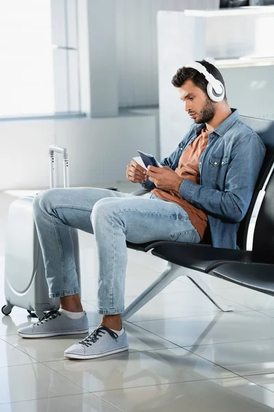 Hombre con auriculares con pasaporte en la sala de salida del aeropuerto - foto de stock