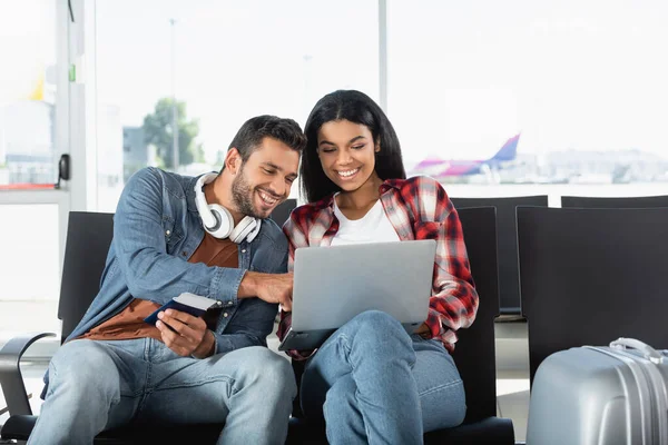 Glückliches gemischtrassiges Paar schaut auf Laptop im Flughafen — Stockfoto