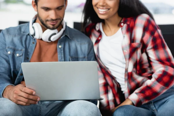 Mann benutzt Laptop in der Nähe von fröhlicher afrikanisch-amerikanischer Frau auf verschwommenem Hintergrund — Stockfoto
