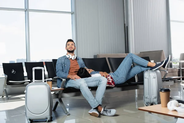 African american woman lying near cheerful man in departure lounge of airport — Stock Photo