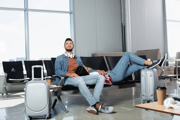 Mulher afro-americana deitado perto de homem alegre na sala de embarque do aeroporto — Fotografia de Stock