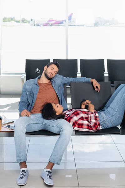 African american woman lying near sleepy man in departure lounge of airport — Stock Photo