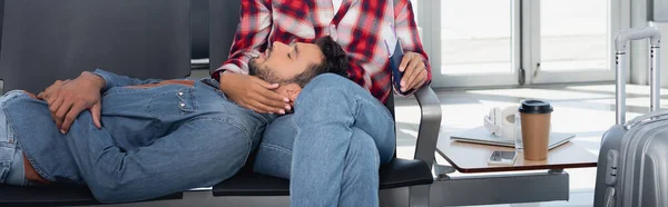 Barbudo hombre acostado en mujer afroamericana en la sala de salida del aeropuerto, pancarta - foto de stock