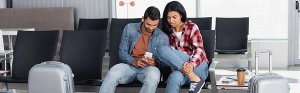 Afrikanisch-amerikanische Frau und bärtiger Mann, der in der Abflughalle des Flughafens auf das Telefon schaut, Banner — Stockfoto