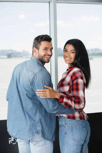 Glückliches multikulturelles Paar lächelt beim Umarmen am Flughafen — Stockfoto