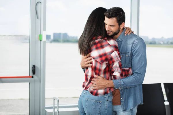 Bearded man hugging brunette african american girlfriend in airport — Stock Photo