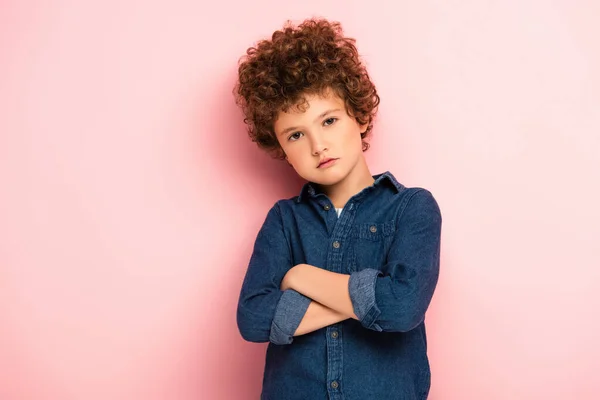 Serious and curly boy standing with crossed arms on pink — Stock Photo