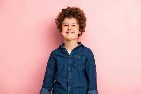 Heureux et bouclé garçon en denim chemise souriant sur rose — Photo de stock