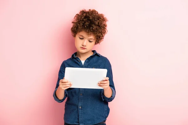 Curly boy in denim shirt using digital tablet on pink — Stock Photo