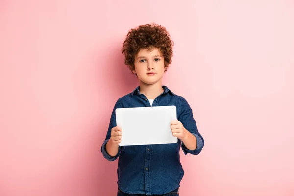 Кучерявий хлопчик у джинсовій сорочці тримає цифровий планшет на рожевому — Stock Photo