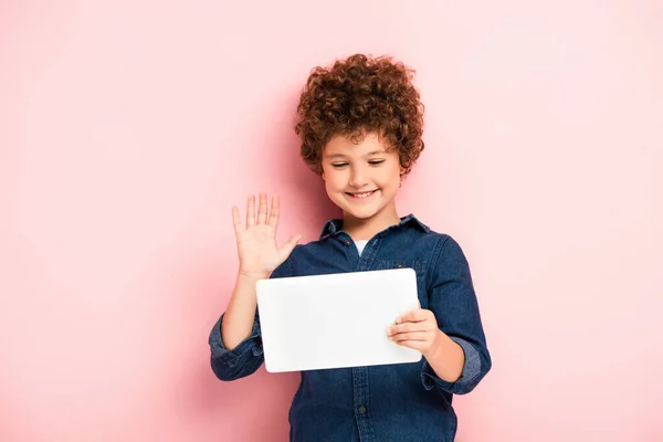 Lockiges Kind winkt mit der Hand, während es ein digitales Tablet während eines Videogesprächs auf rosa benutzt — Stockfoto