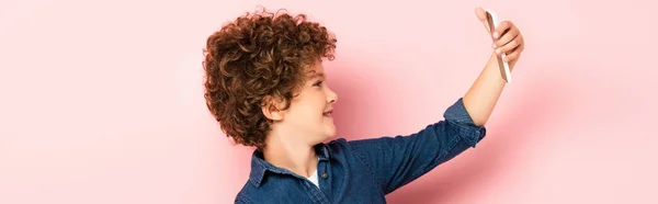 Panoramische Ernte von lockigem Kind in Jeanshemd macht Selfie auf Smartphone auf rosa — Stockfoto