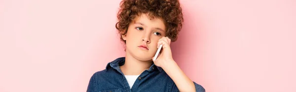 Horizontal image of curly boy in denim shirt talking on smartphone on pink — Stock Photo