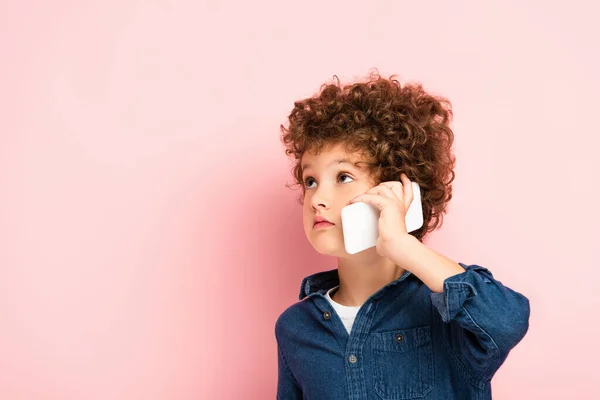 Curly boy in denim shirt talking on cellphone on pink — Stock Photo