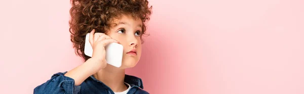 Horizontal concept of curly boy in denim shirt talking on mobile phone and looking away on pink — Stock Photo