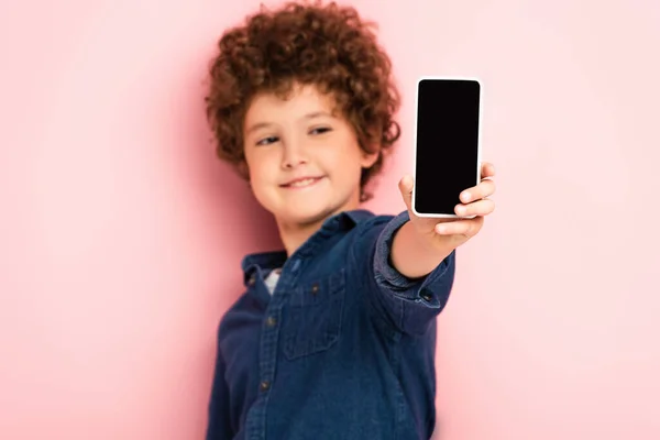 Selective focus of curly child in denim shirt holding smartphone with blank screen on pink — Stock Photo