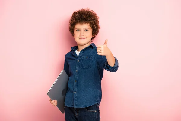 Joyful boy holding laptop and showing thumb up on pink — Stock Photo