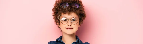 Panoramic shot of curly boy in bunch of eyeglasses looking at camera on pink — Stock Photo