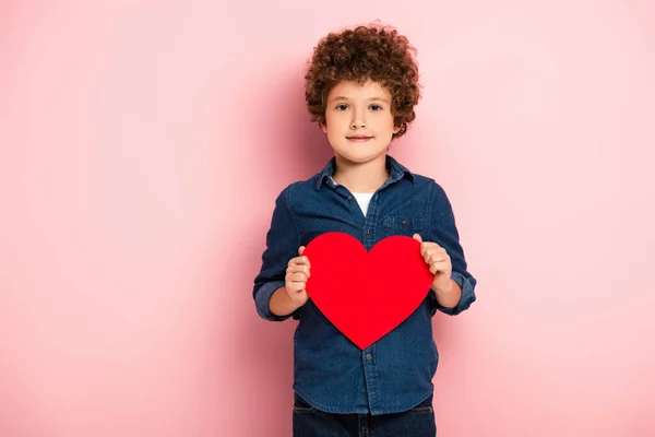 Joyful boy holding heart shape paper cut on pink — Stock Photo