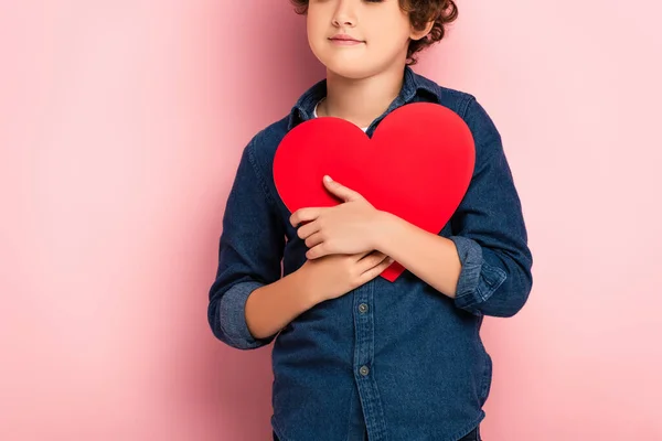 Cropped view of boy holding heart shape paper cut on pink — Stock Photo