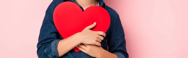 Panoramic crop of boy holding heart shape paper cut on pink — Stock Photo