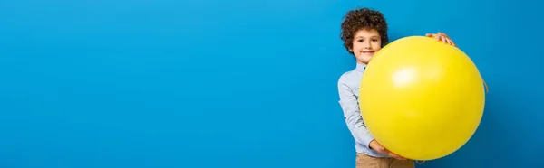 Panoramic crop of pleased boy holding big yellow balloon on blue — Stock Photo