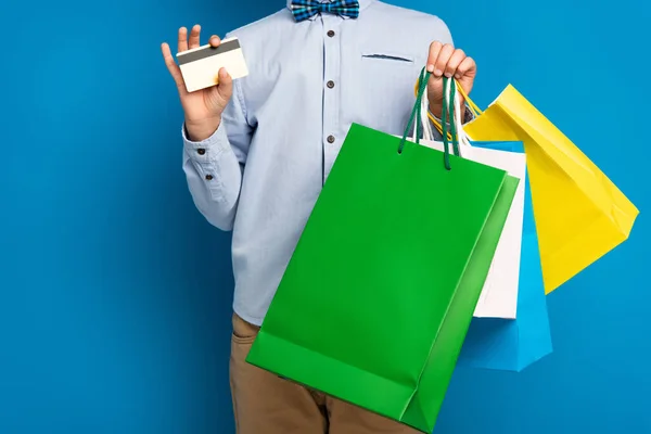 Vista recortada de niño sosteniendo bolsas de compras y tarjeta de crédito en azul - foto de stock