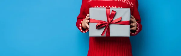 Horizontal crop of boy in red sweater with ornament holding present on blue — Stock Photo
