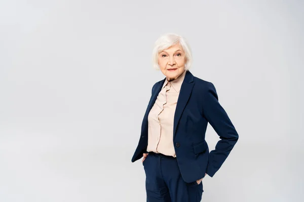 Senior woman looking at camera while standing with hands in pockets of pants isolated on grey — Stock Photo