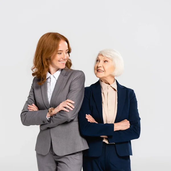 Mujeres de negocios sonrientes con los brazos cruzados mirándose aisladas en gris - foto de stock