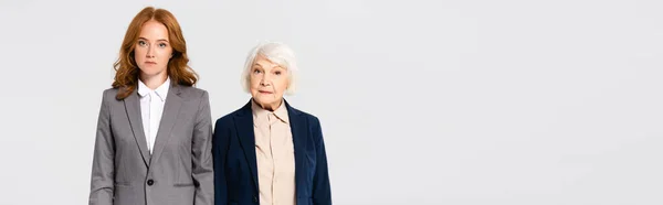 Red haired and senior businesswomen looking at camera isolated on grey, banner — Foto stock