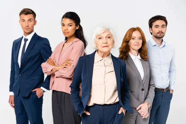 Senior empresaria mirando la cámara cerca de colegas multiculturales aislados en gris - foto de stock