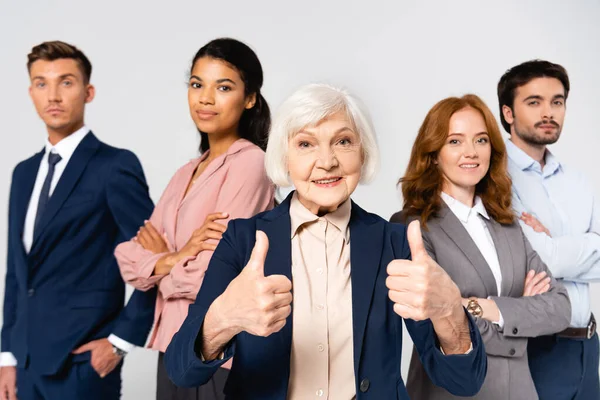 Femme d'affaires souriante montrant comme des gens d'affaires presque multiculturels sur fond flou isolé sur gris — Photo de stock