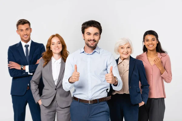 Lächelnder Geschäftsmann zeigt Daumen hoch neben fröhlichen multiethnischen Kollegen, die in grau isoliert sind — Stockfoto