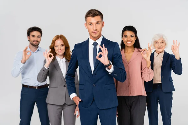 Smiling multicultural businesspeople showing ok gesture isolated on grey - foto de stock