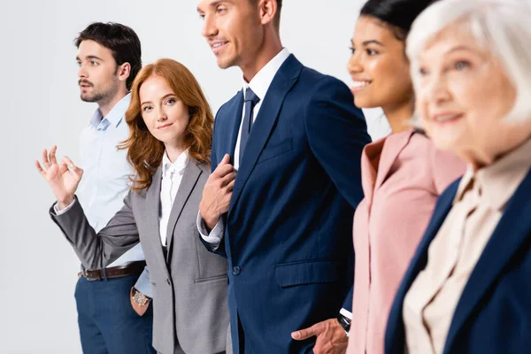 Businesswoman showing ok gesture near smiling multiethnic colleagues on blurred foreground isolated on grey — Stock Photo