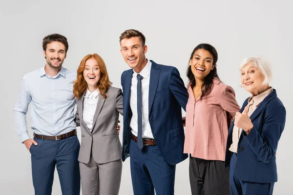 Cheerful multiethnic businesspeople embracing and showing like gesture isolated on grey — Stock Photo
