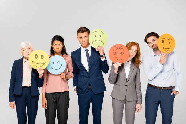 Sad multicultural businesspeople holding cards with emotions isolated on grey — Stock Photo