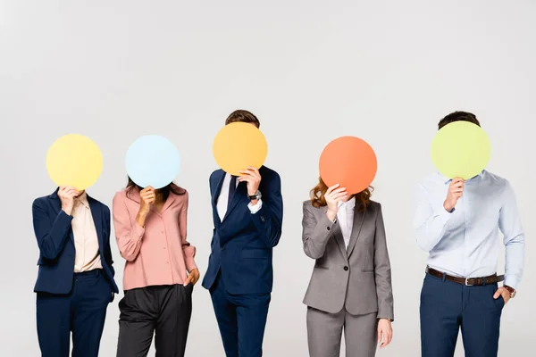 Empresarios multiétnicos cubriendo rostros con tarjetas aisladas en gris - foto de stock
