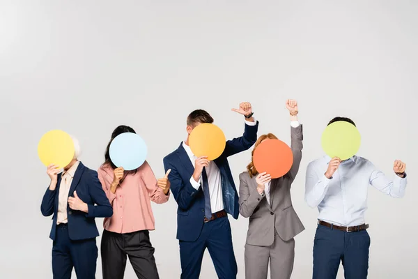 Empresarios multiculturales mostrando como gesto mientras cubren rostros con tarjetas aisladas en gris - foto de stock