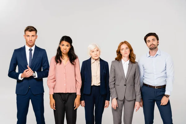 Pensive multiethnic businesspeople looking at camera isolated on grey — Stock Photo