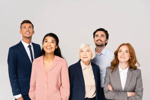 Negocios multiculturales sonrientes mirando hacia arriba aislados en gris - foto de stock