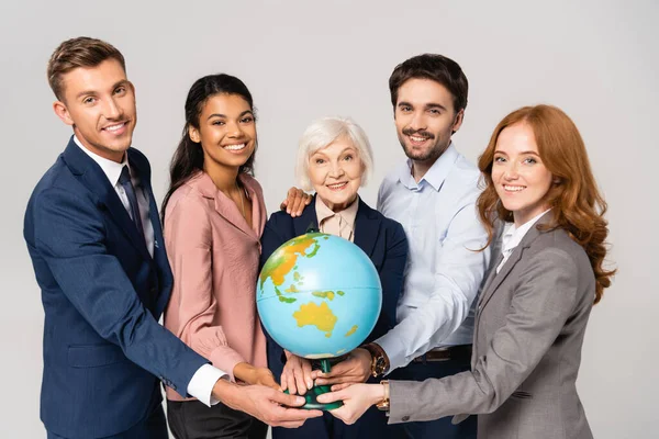 Imprenditori multiculturali che tengono il globo sorridendo isolati sul grigio — Foto stock