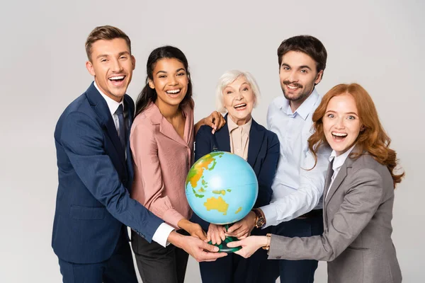 Allegro uomini d'affari multietnici in possesso di globo, mentre guardando la fotocamera isolata su grigio — Foto stock